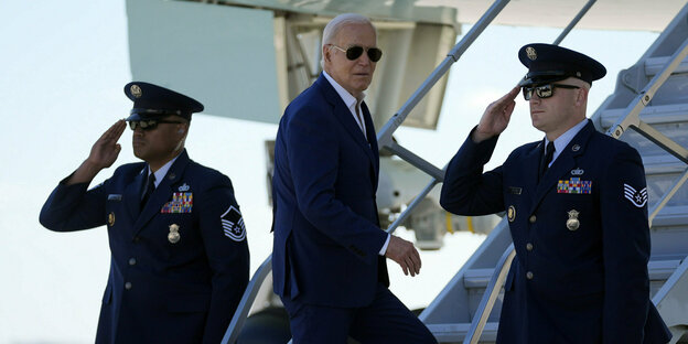 Präsident Biden klettert in ein Flugzeug, flankiert von zwei Soldaten